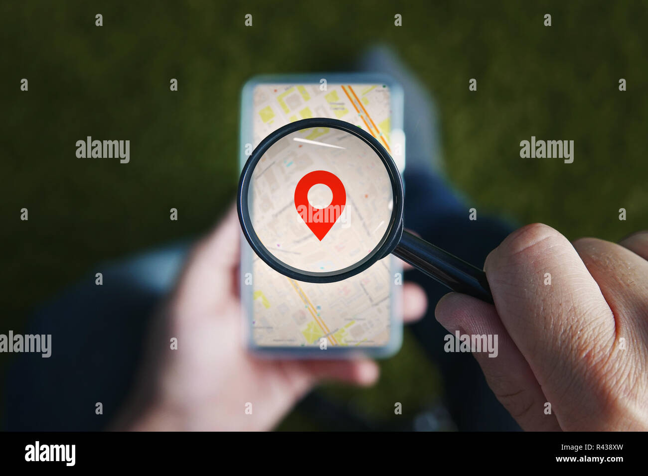 Shot of male hands holding magnifying glass with the red icon of geo-location and looking through it to the smartphone with online city map on the screen. Concept of using mobile net for navigation. Stock Photo