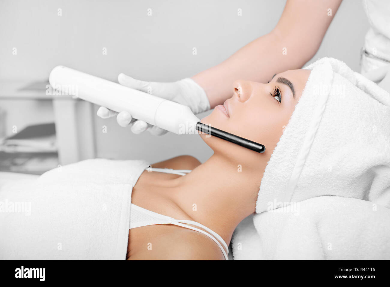 woman getting electric darsonval facial massage procedure at beauty salon. Stock Photo
