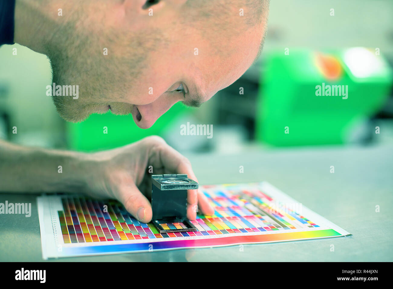 Worker in a printing and press center uses a magnifying glass to check the print quality. Scene