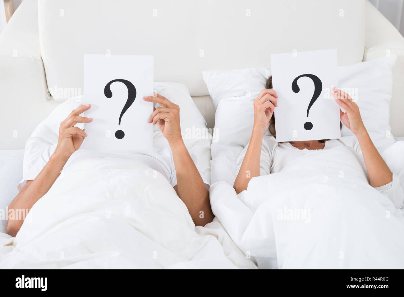 Couple Holding Question Mark Over Faces Stock Photo