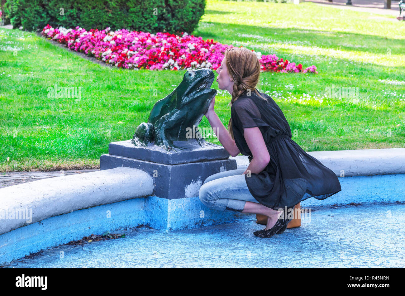young woman kisses frog sculpture. Stock Photo