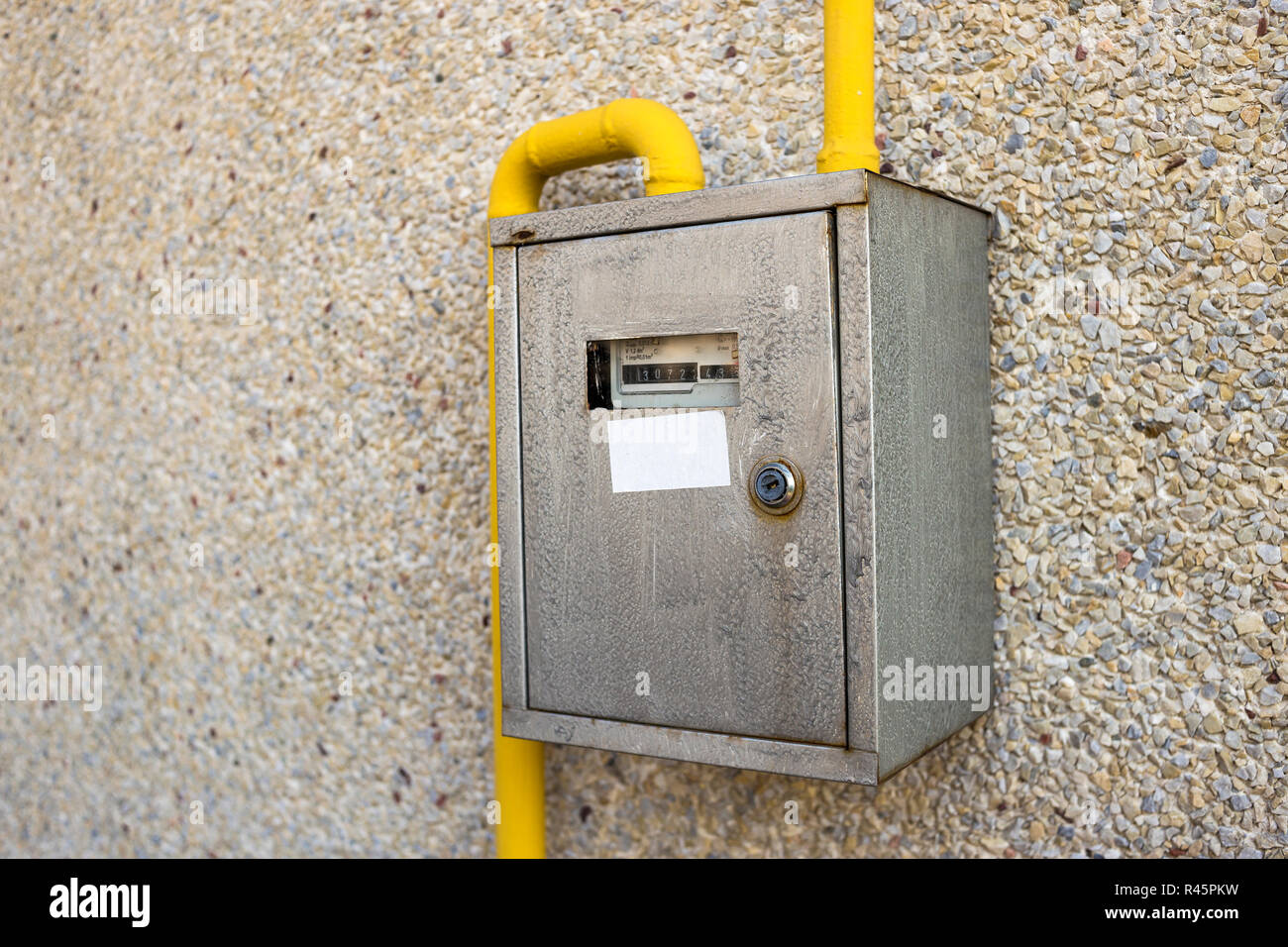 Close-up of metal steel gas meter box with connecting yellow pipes hanging on exterior light stone house wall. Construction, renovation, measurement t Stock Photo