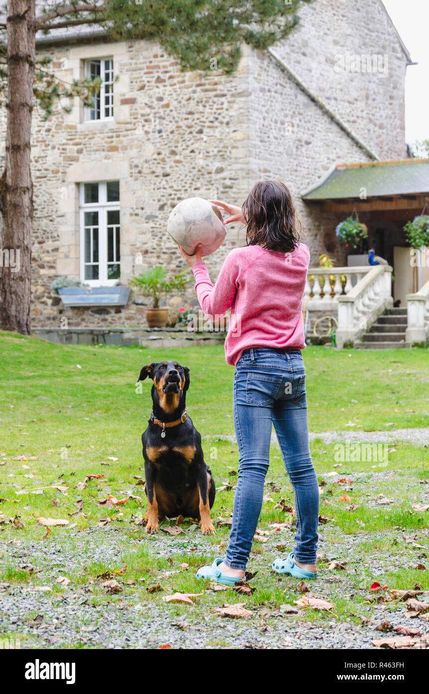 Girl holding a ball and playing with black dog in backyard of big country house Stock Photo