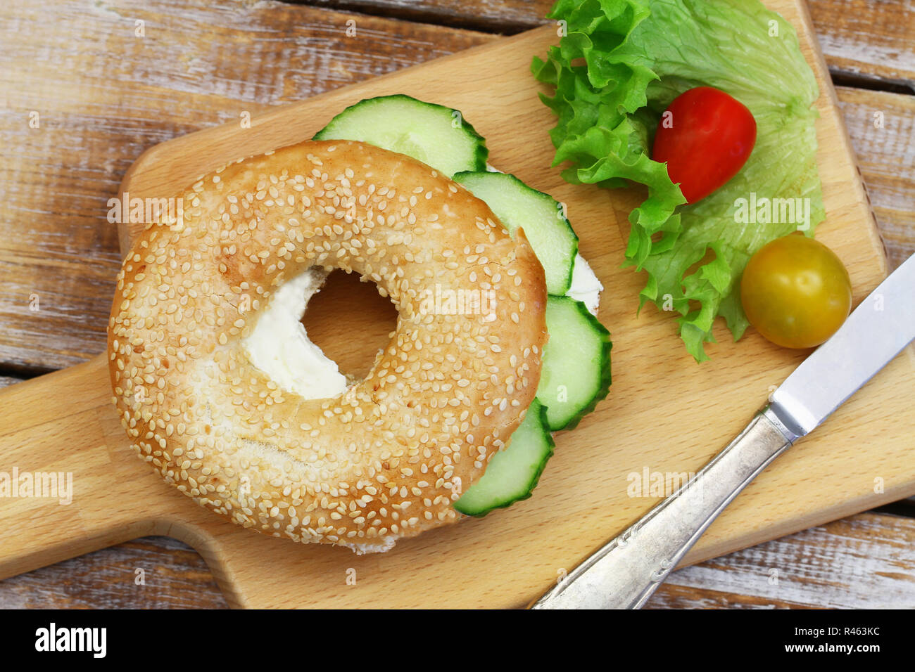 White sesame bagel with cream cheese and cucumber and cherry tomatoes on wooden board Stock Photo