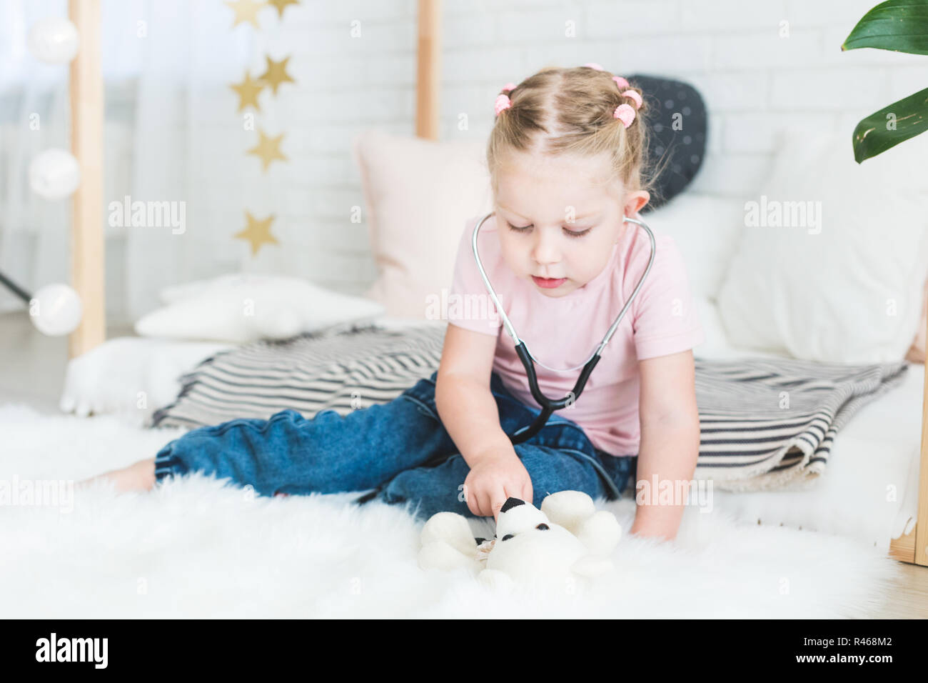Cute little girl sitting on the bed and playing doctor with stethoscope and Teddy Bear. Stock Photo