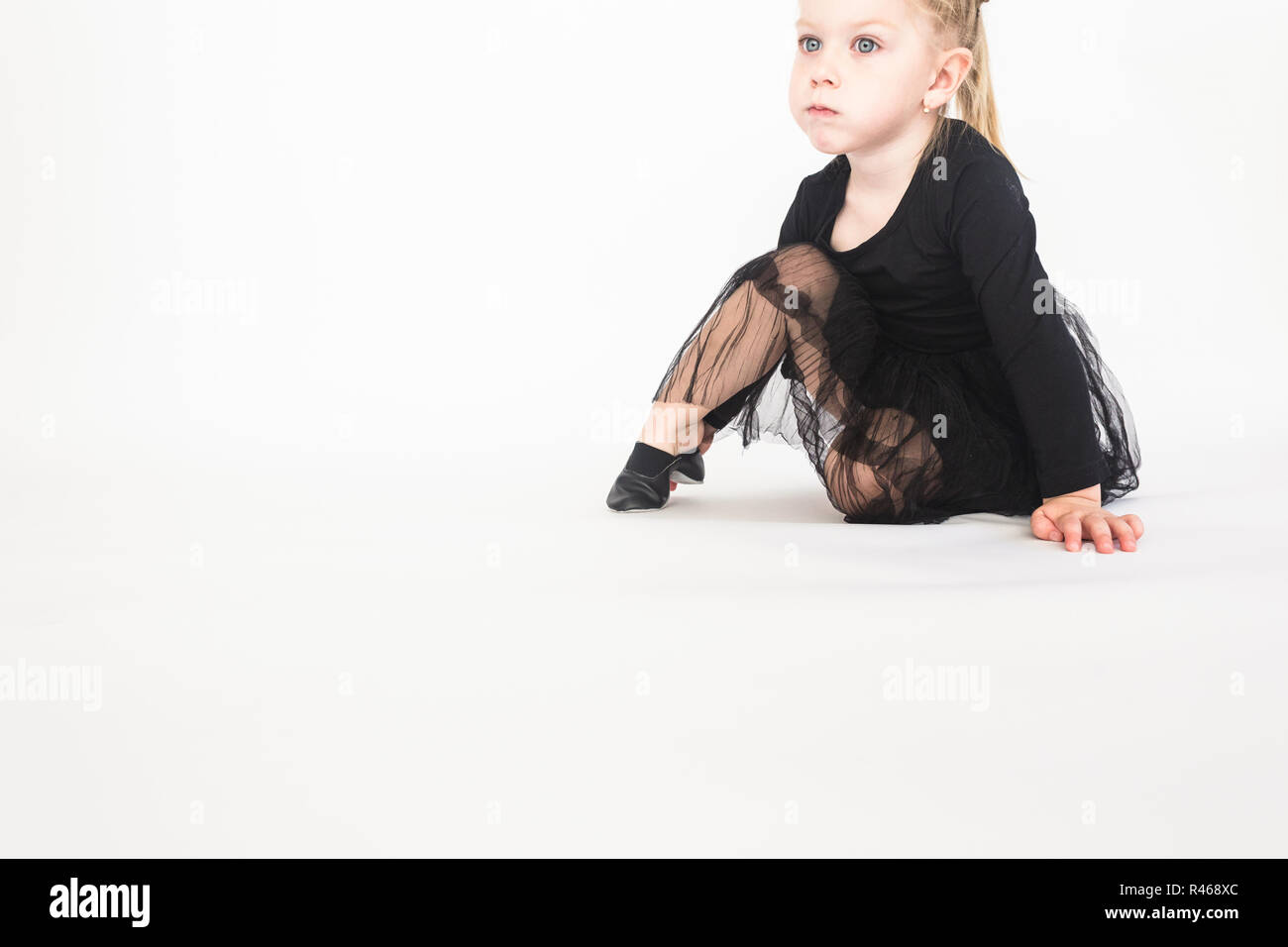 Cute little girl in beautiful black dress sitting on the floor on white ...