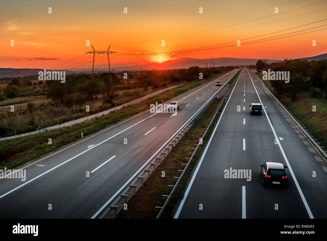 Light Highway Traffic On A Straight Road At Dramatic Orange Sunset Through Pastoral Landscape Stock Photo Alamy