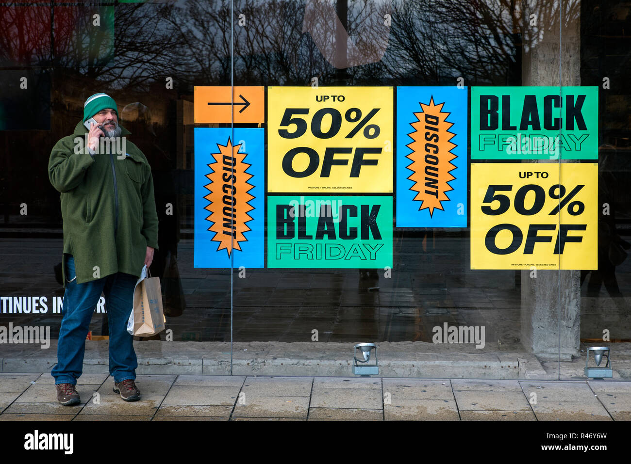 Man on the phone beside Black Friday 50% off signs in the window of Urban Outfitters on Princes Street, Edinburgh, Scotland, UK. Stock Photo