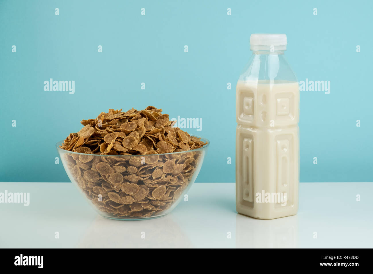 Helathy vegetarian breakfast concept. Bowl full of cereals and bottle of milk on white table and blue background Stock Photo