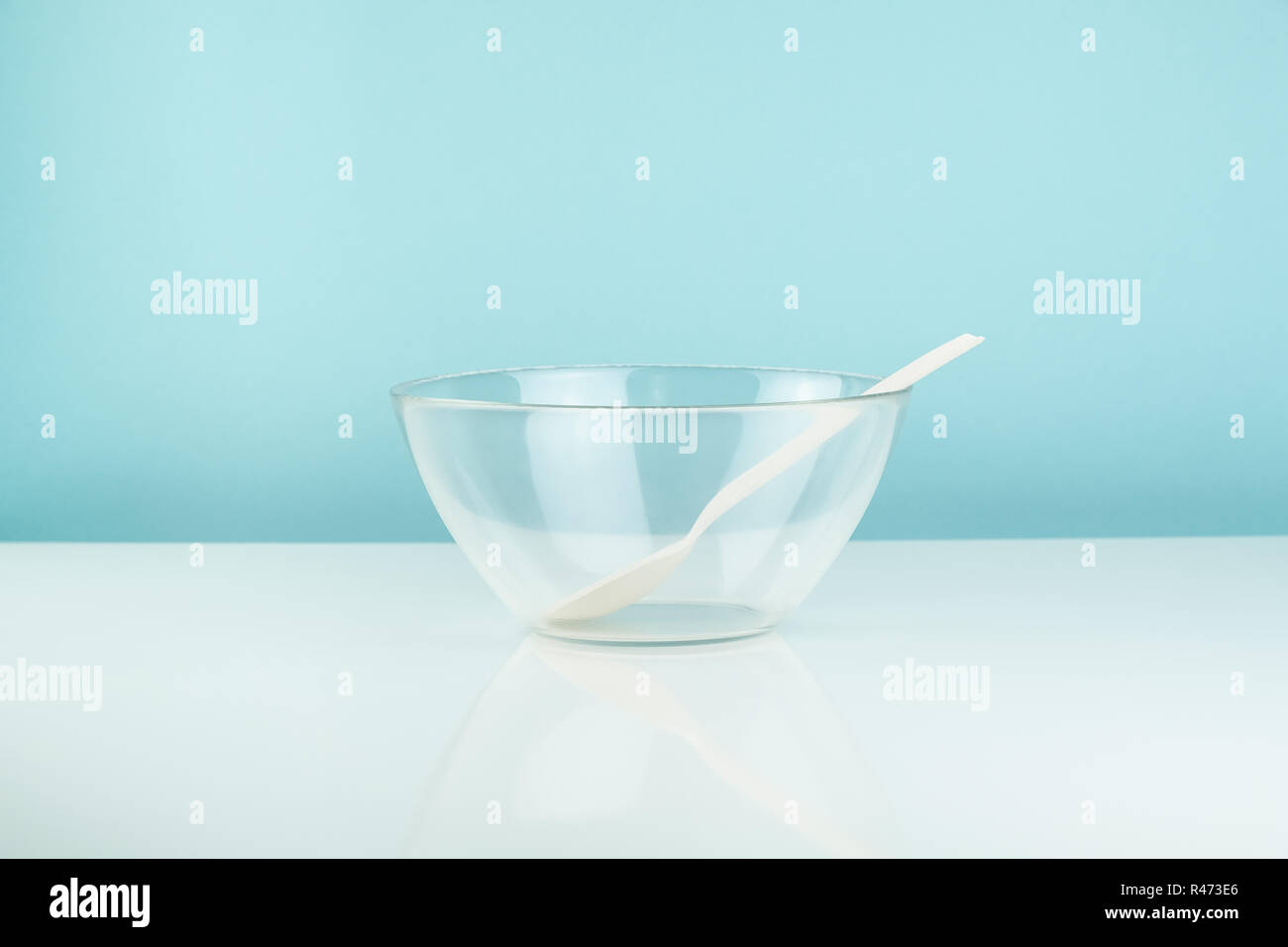 Empty glass bowl and spoon on a table. Hunger or diet concept: clean transparrent dinnerware in white and blue background Stock Photo