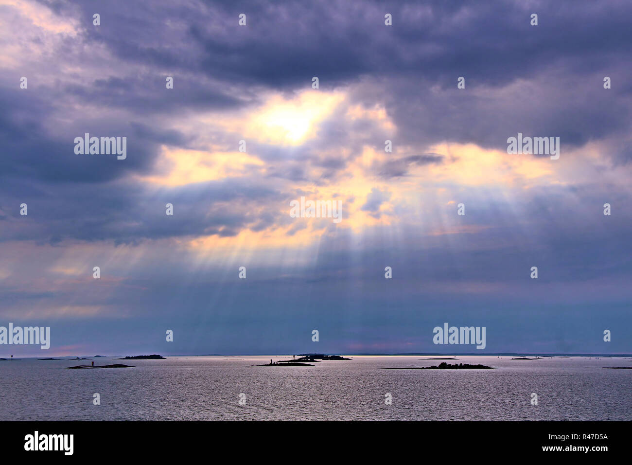 The sun behind the clouds with rays of light shining down on sea Stock Photo