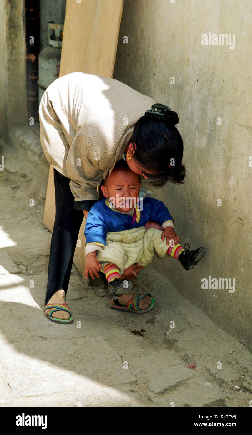 Tibet, Lhasa: Weinender kleiner Junge wird von seiner Mutter zum Pipi machen durch den bei Kleinkinder ¸blichen Hosenschlitz ¸ber der Straﬂe abgehalte Stock Photo