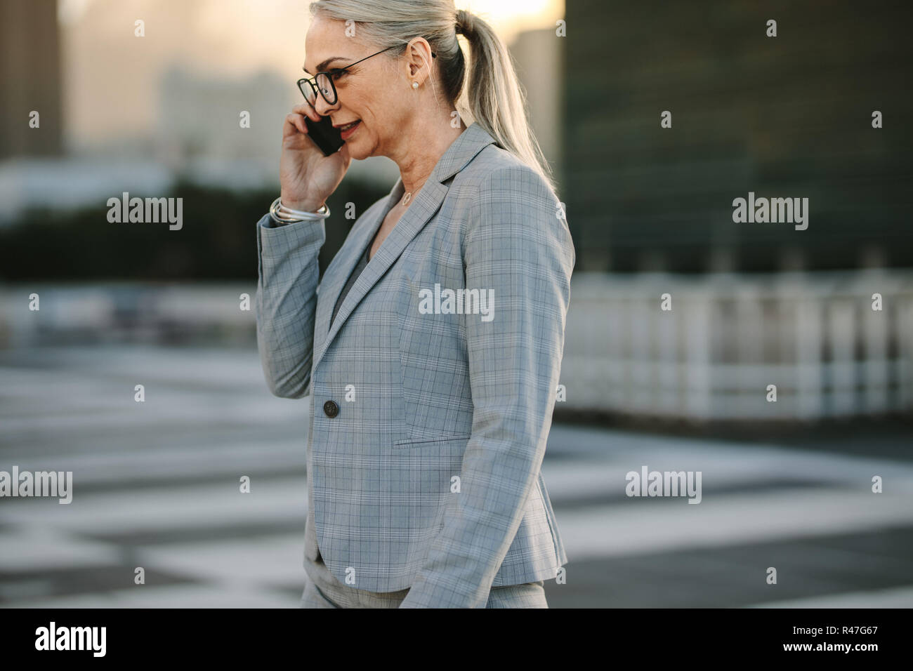 Mature businesswoman on way to home using phone. Senior executive walking on city street talking on cellphone during evening. Stock Photo