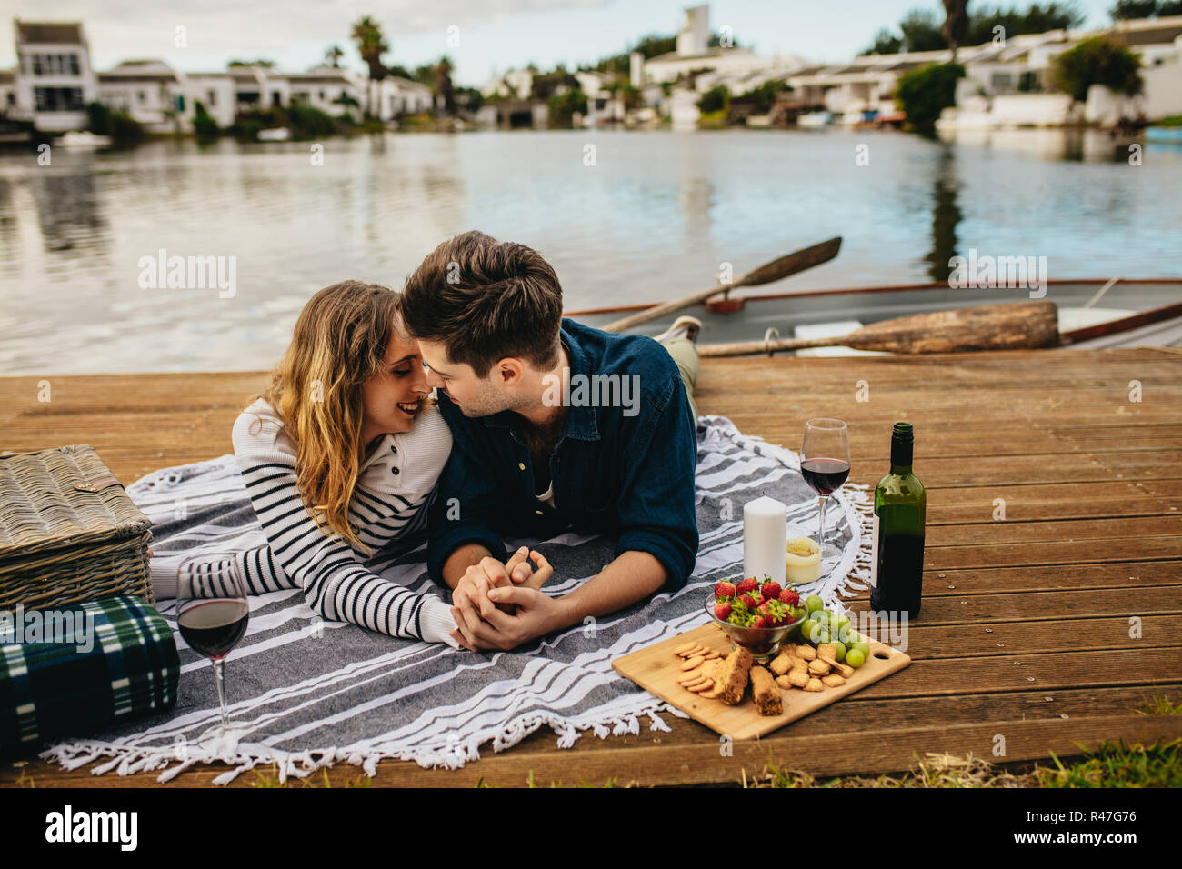 Romantic couple on a date kissing and spending time together lying near a lake. Man kissing his girlfriend lying on a wooden dock near a lake holding  Stock Photo