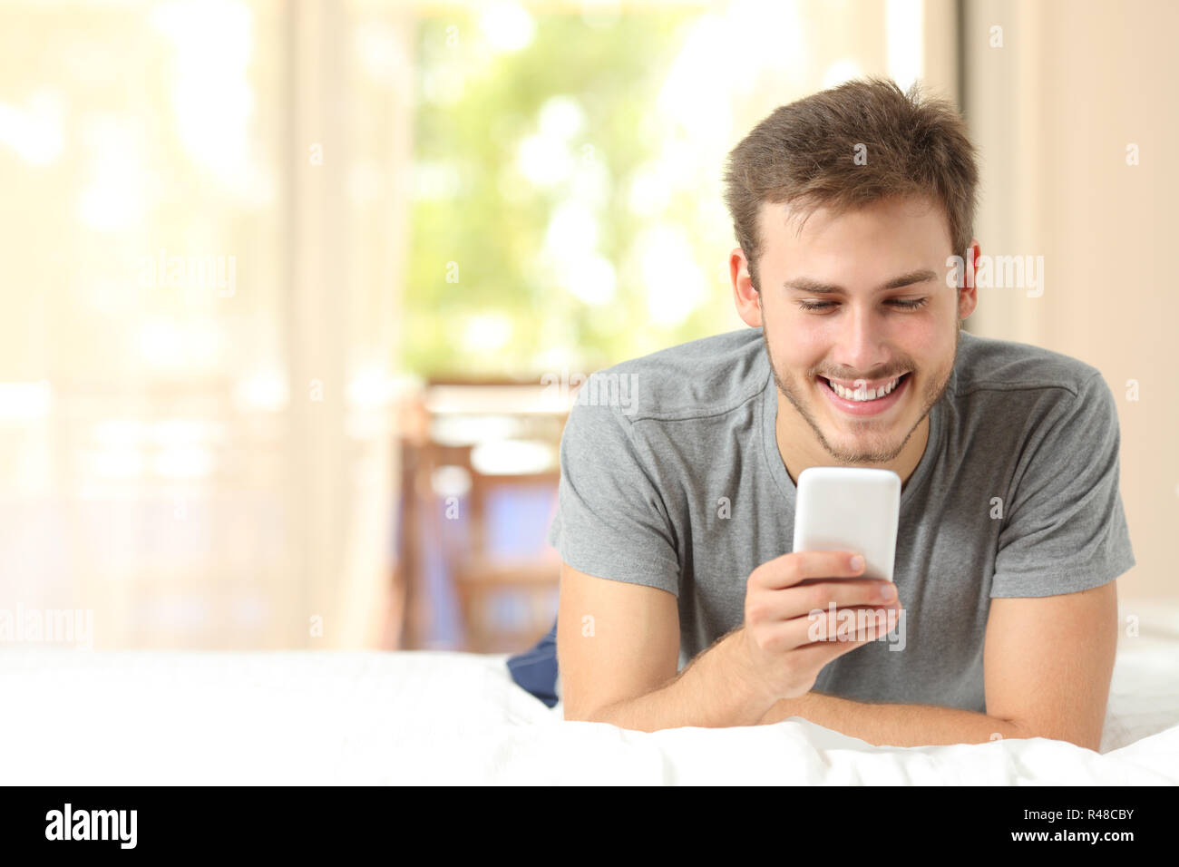 Guy using a mobile phone on a bed at home Stock Photo