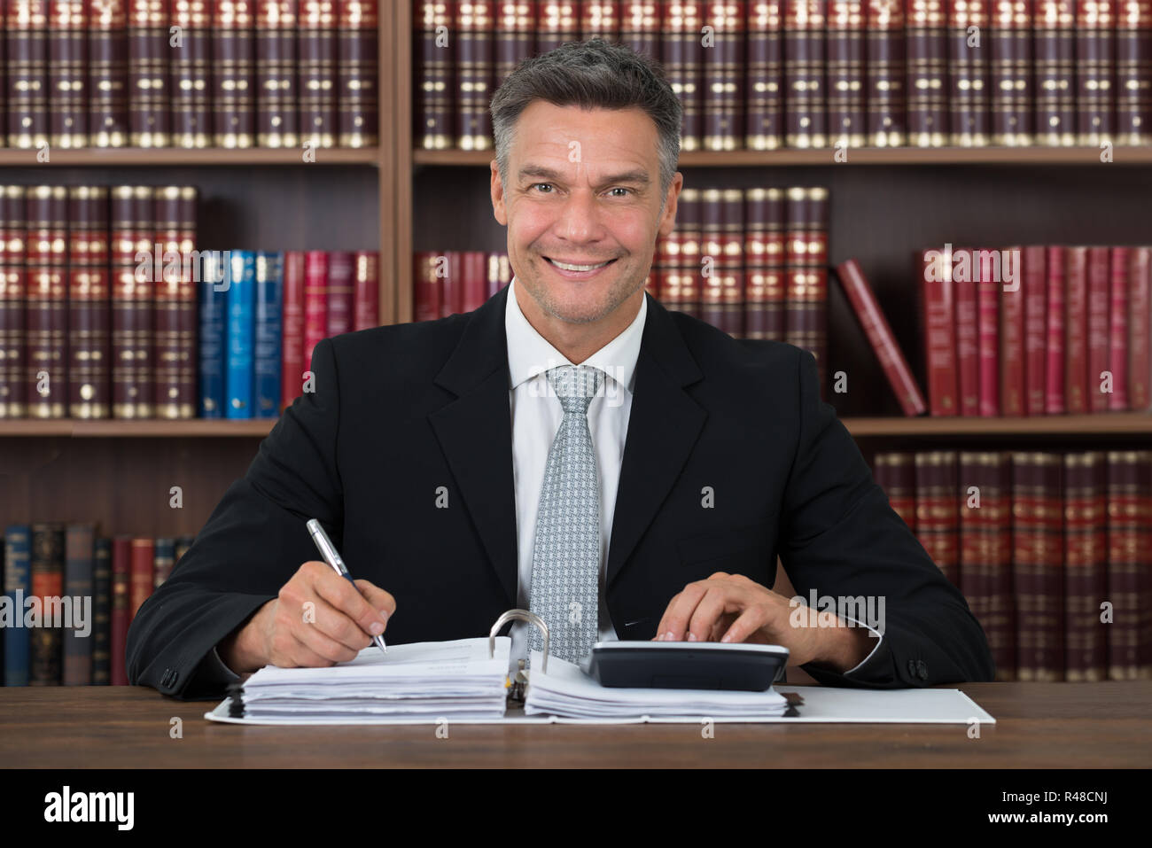 Accountant Writing On Document While Using Calculator At Table Stock Photo