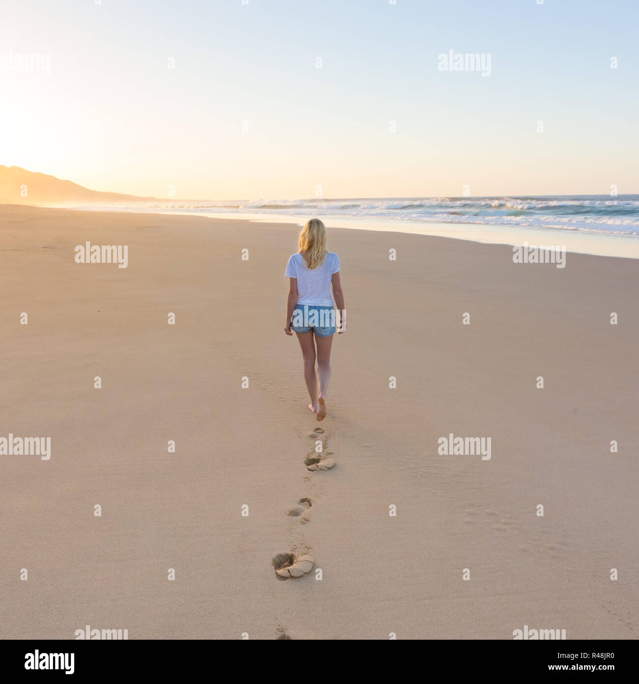 Lady walking on sandy beach in sunset leaving footprints behind Stock ...
