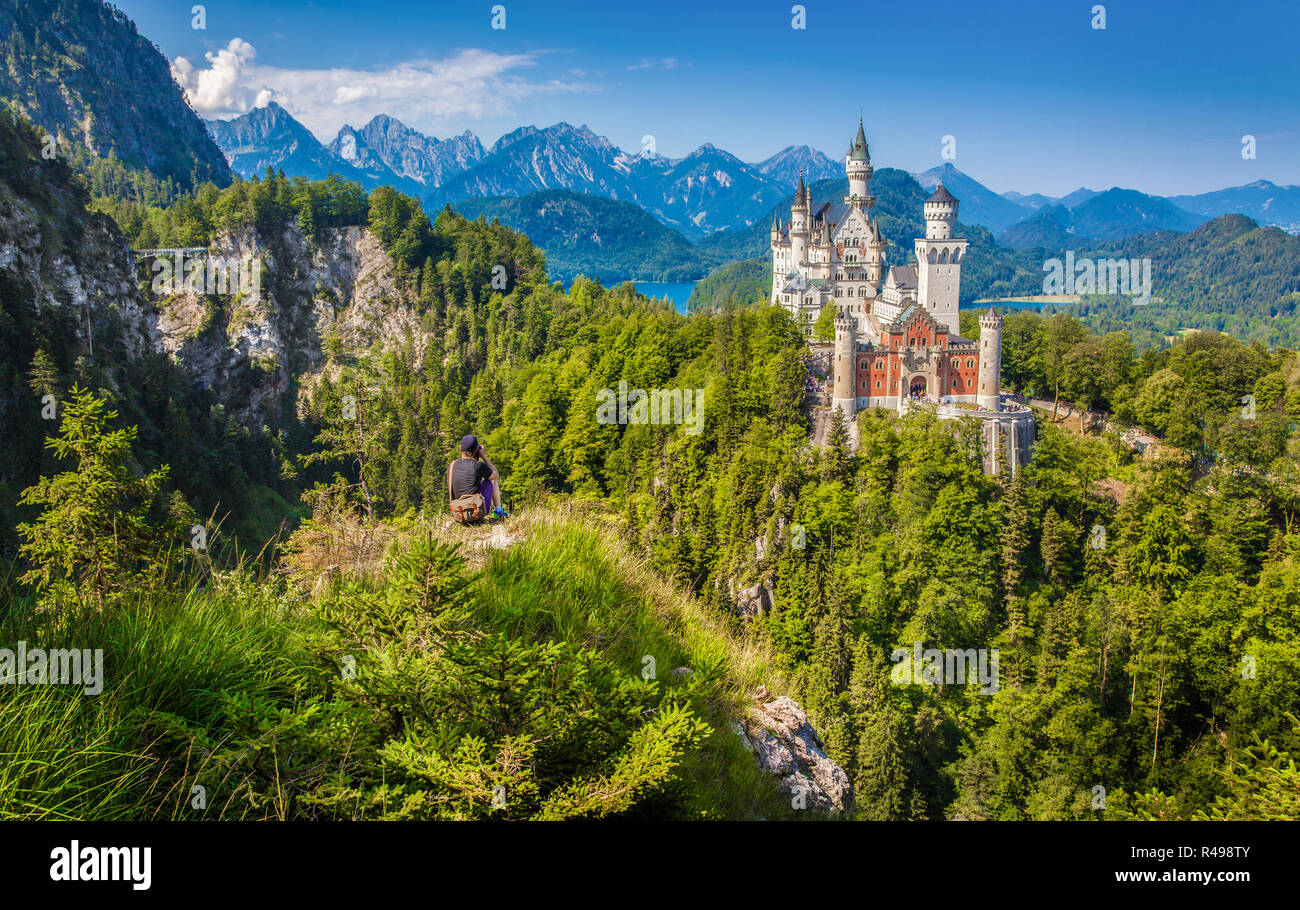 Classic view of famous Neuschwanstein Castle with male tourist enjoying the view from a steep cliff, Füssen, Bavaria, Germany Stock Photo