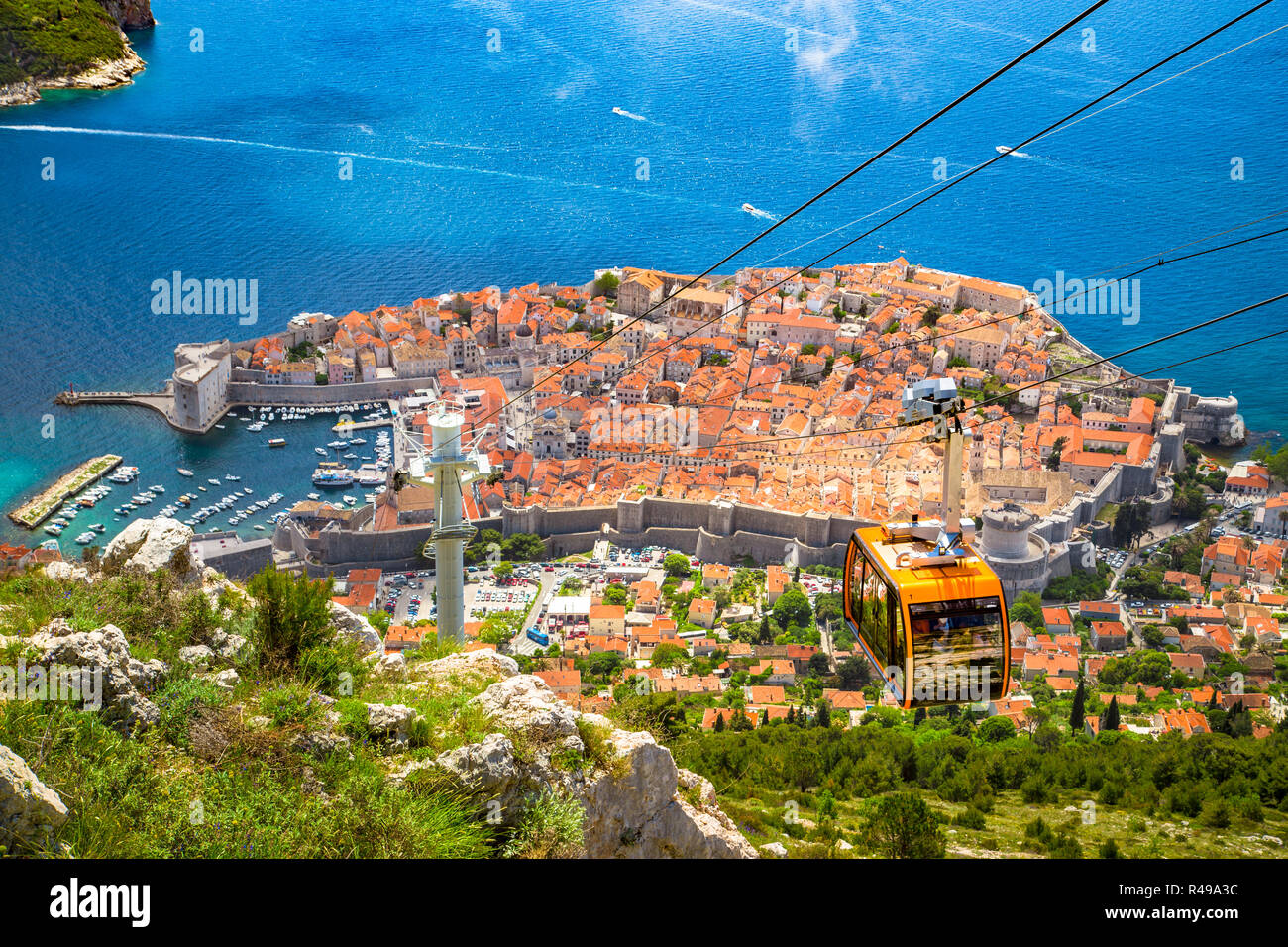 Aerial panoramic view of the old town of Dubrovnik with famous Cable Car on Srd mountain on a sunny day with blue sky and clouds in summer, Dalmatia,  Stock Photo