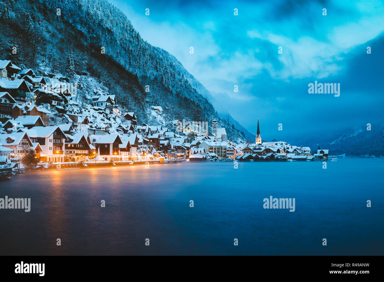 Panorama view of famous Hallstatt lakeside town in the Alps in mystic twilight during blue hour at dawn on a beautiful cold foggy day in winter, Salzk Stock Photo