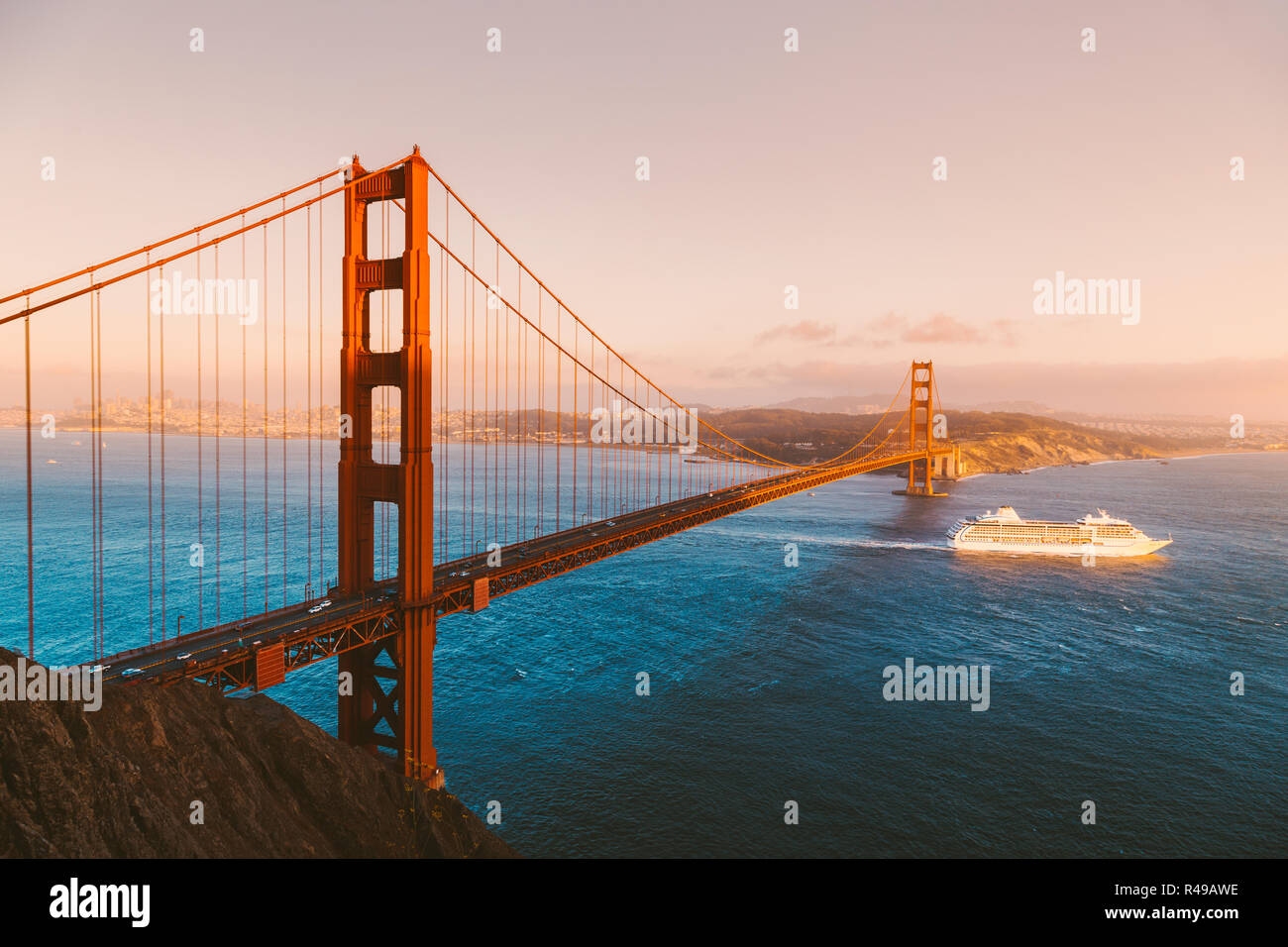 Beautiful panorama view of cruise ship passing famous Golden Gate Bridge with the skyline of San Francisco in the background at sunset, California, US Stock Photo