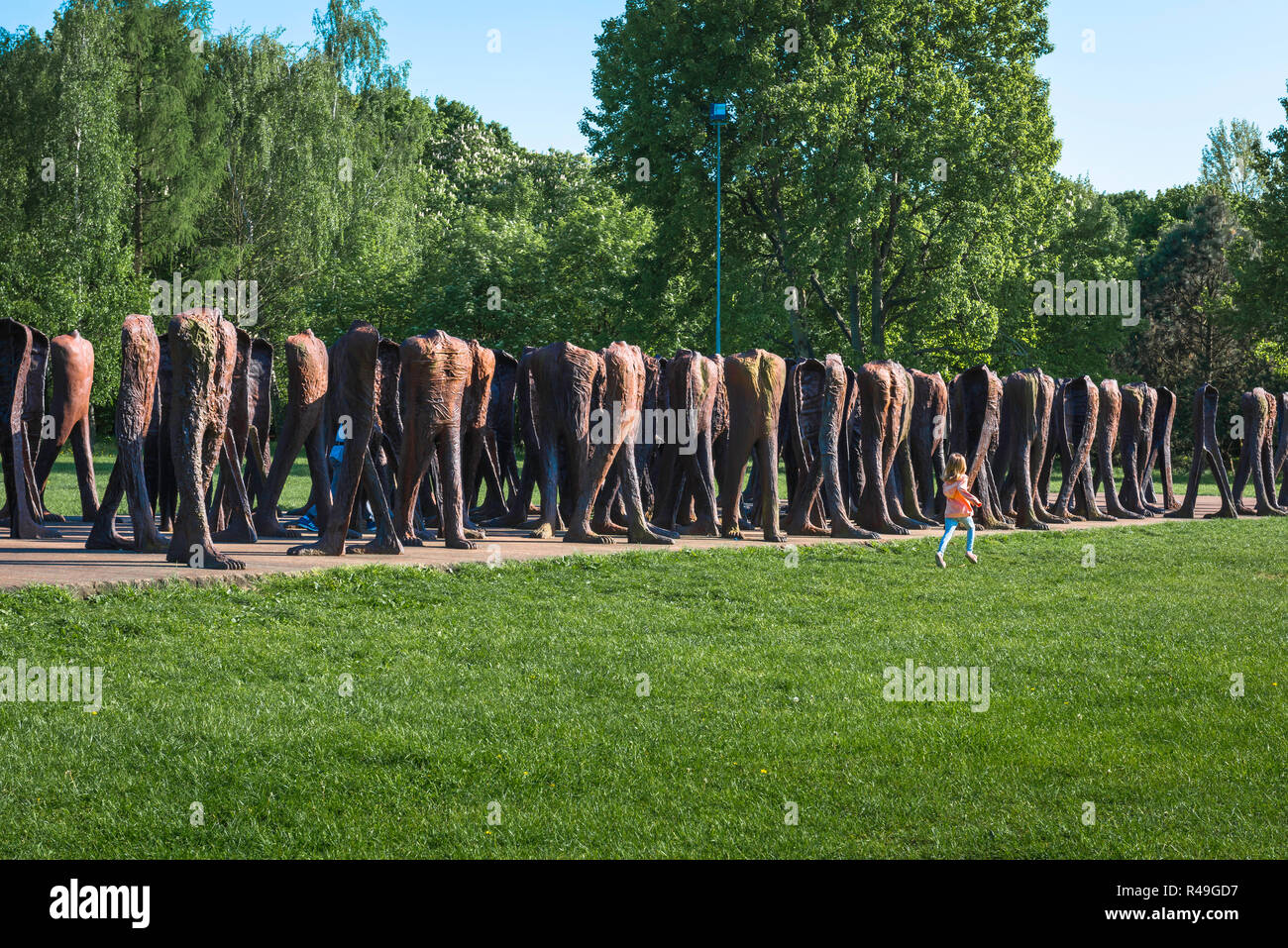 Freedom hope liberty, rear view of child running past a sculpture by Magdalena Abakanowicz (The Unrecognised Ones 2002) in Citadel Park, Poznan Poland Stock Photo