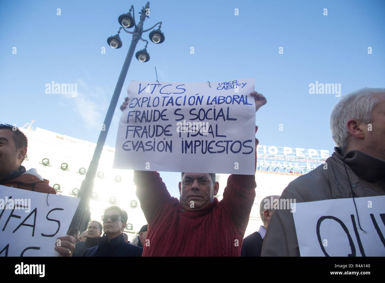 Madrid, Spain. 26th Nov, 2018. Taxi driver carries a placard that denounces the employment situation of Uber or Cabify drivers, during the protest.Some 5,000 taxi drivers led by a fleet of taxi cars protested to demand from the Community and the City Council of the capital the ''immediate and effective'' regulation of the vehicle rental sector with driver (VTC) such as Uber or Cabify. The demonstration has begun at the government headquarters of the Community of Madrid at Puerta del Sol and has ended at Plaza de Cibeles in front of Madrid City Hall. (Credit Image: © Lito Lizana/SOPA Imag Stock Photo