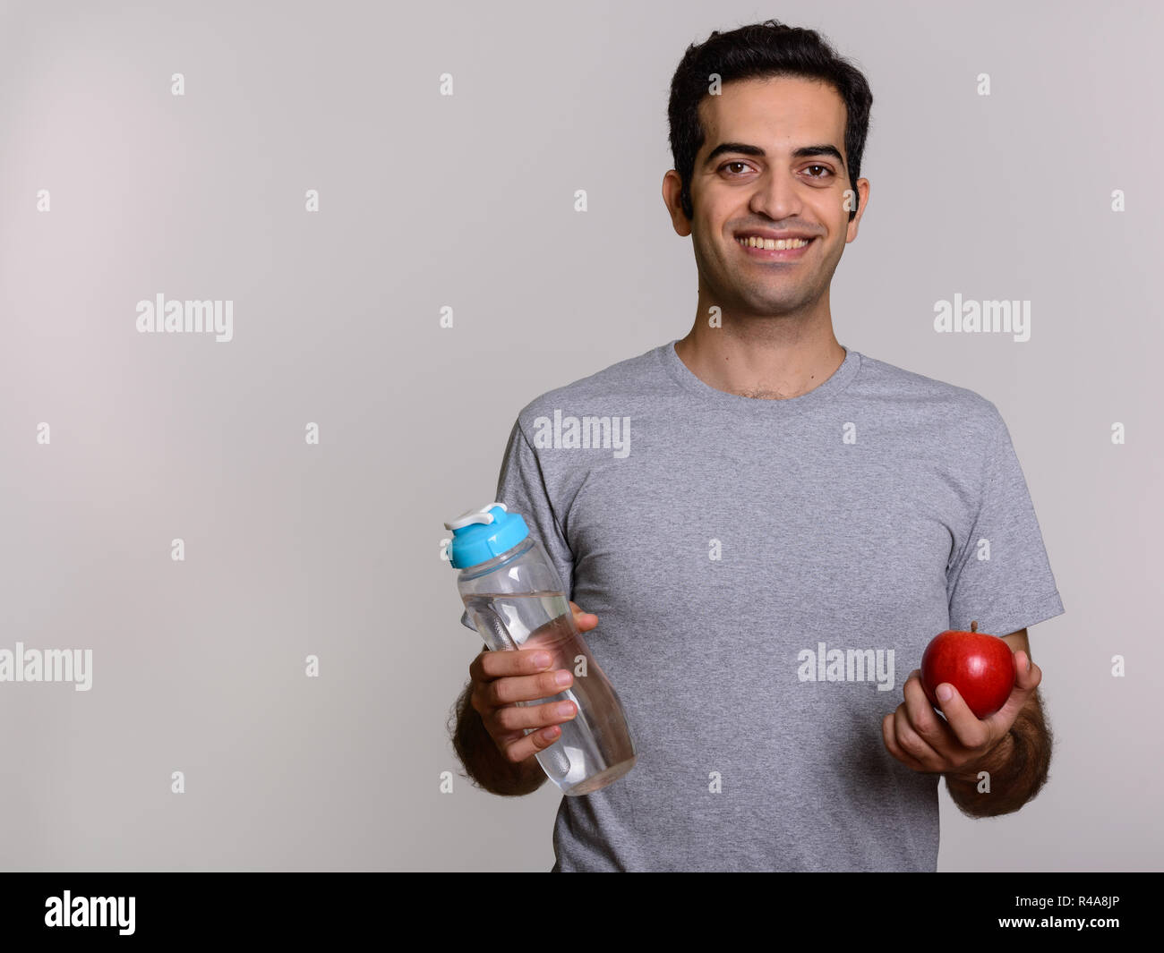 Young happy Persian man holding water bottle and red apple ready Stock ...