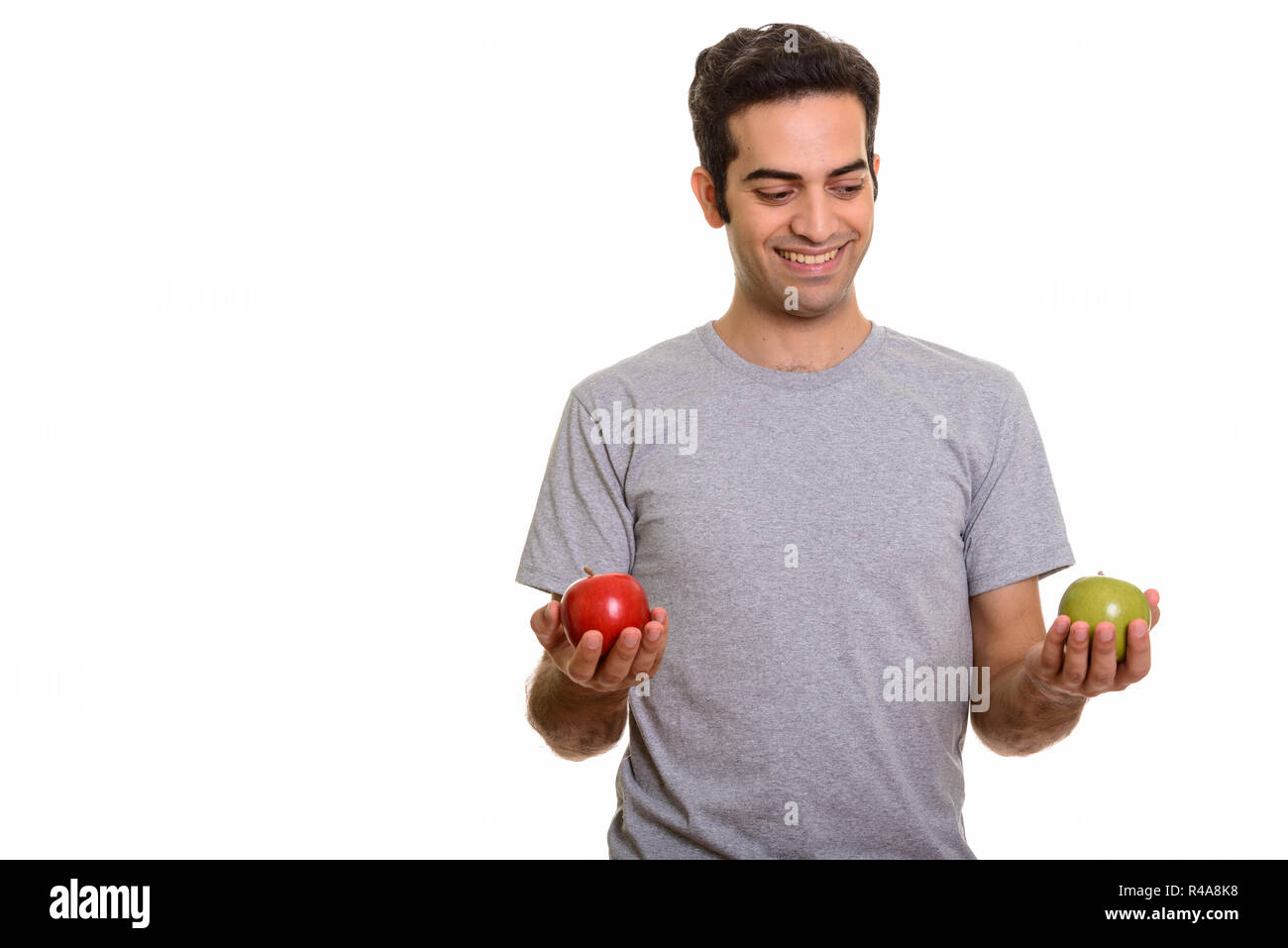 Young happy Persian man choosing between red and green apple rea Stock ...