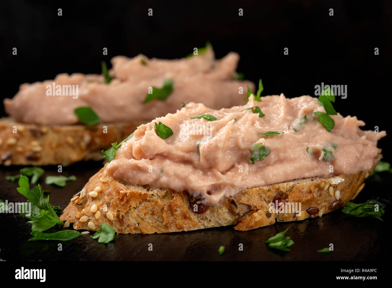 Two slices of bread with vegetable pate and chopped green parsley on a dark slate Stock Photo