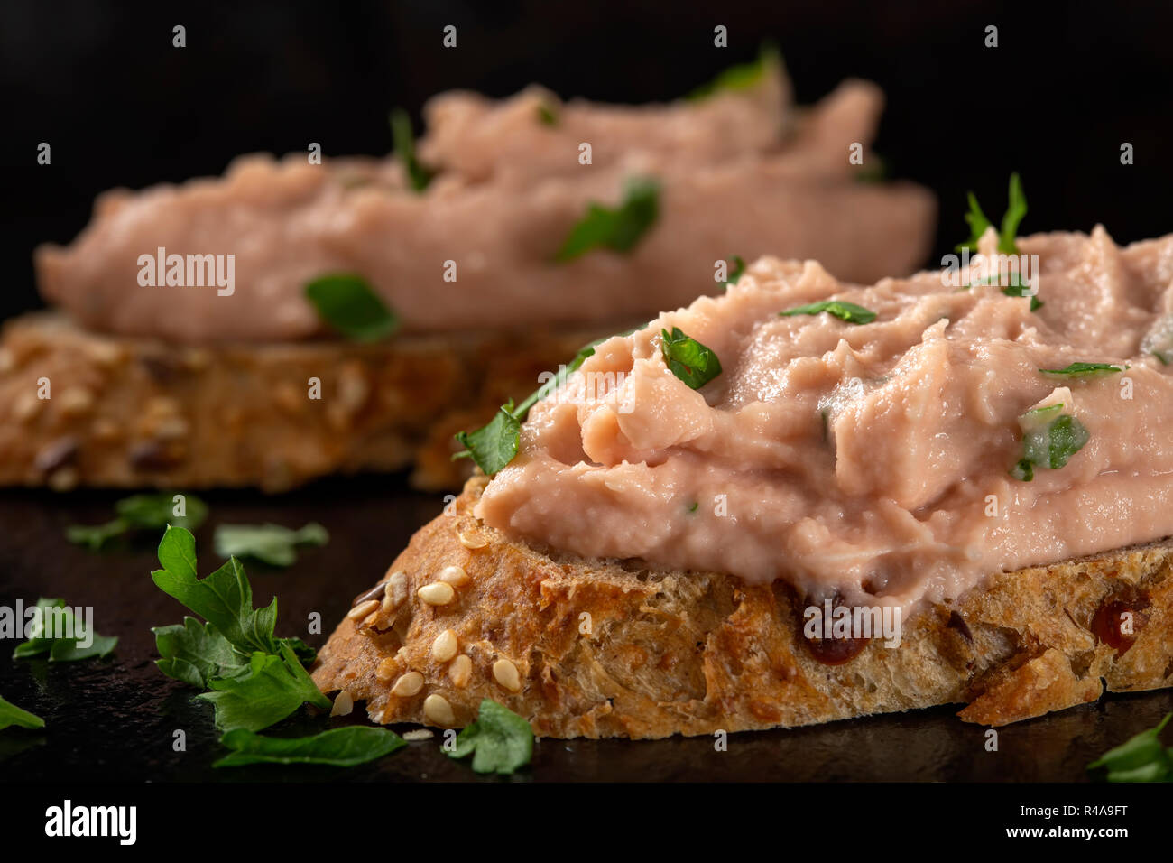 Two slices of bread with vegetable pate and chopped green parsley on a dark slate - close up view Stock Photo