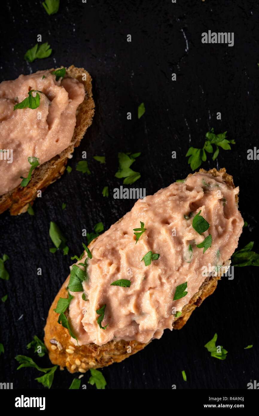Two slices of bread with vegetable pate and chopped green parsley on a dark slate - top view Stock Photo