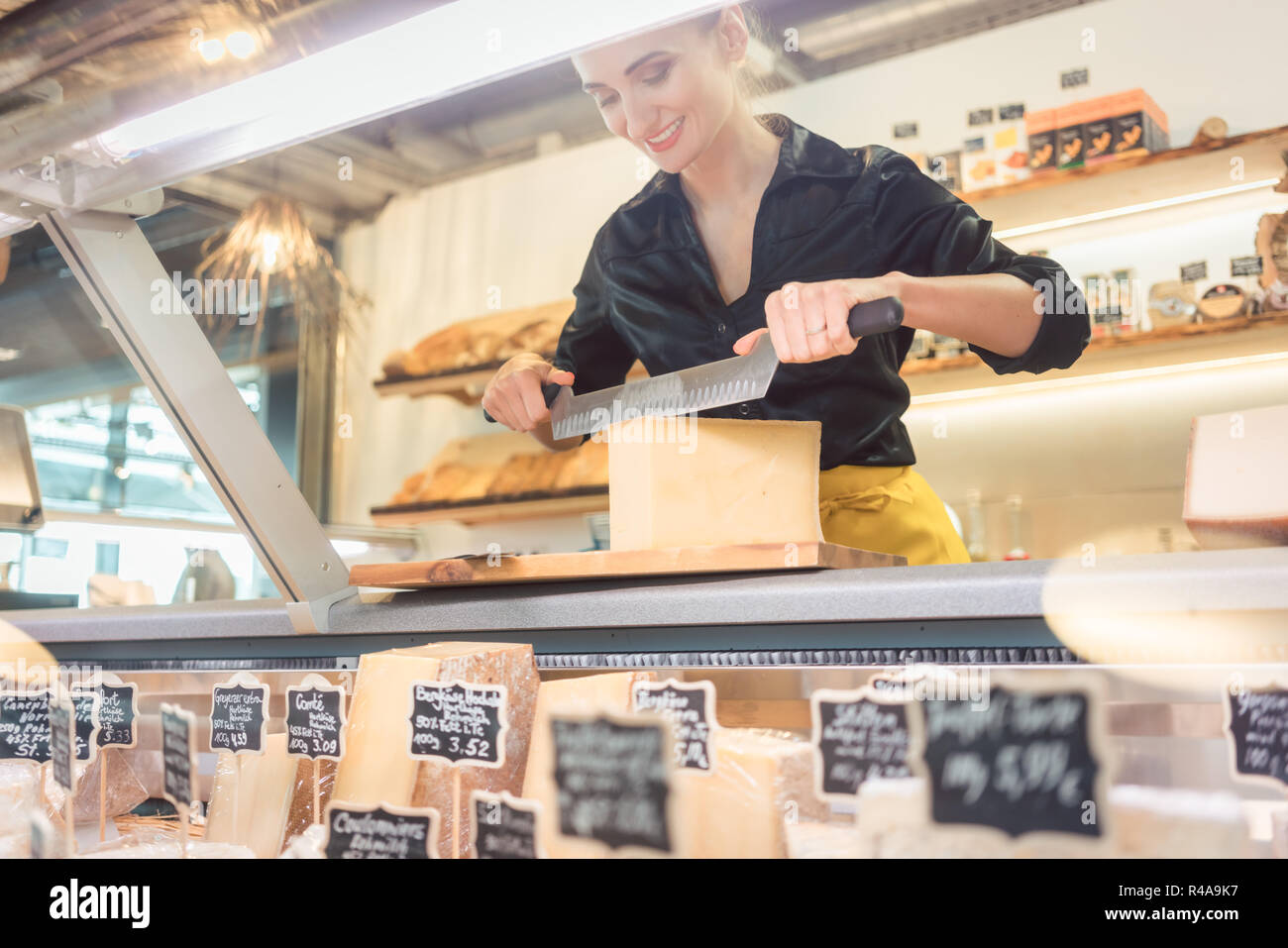 Young shop clerk in deli cutting cheese Stock Photo