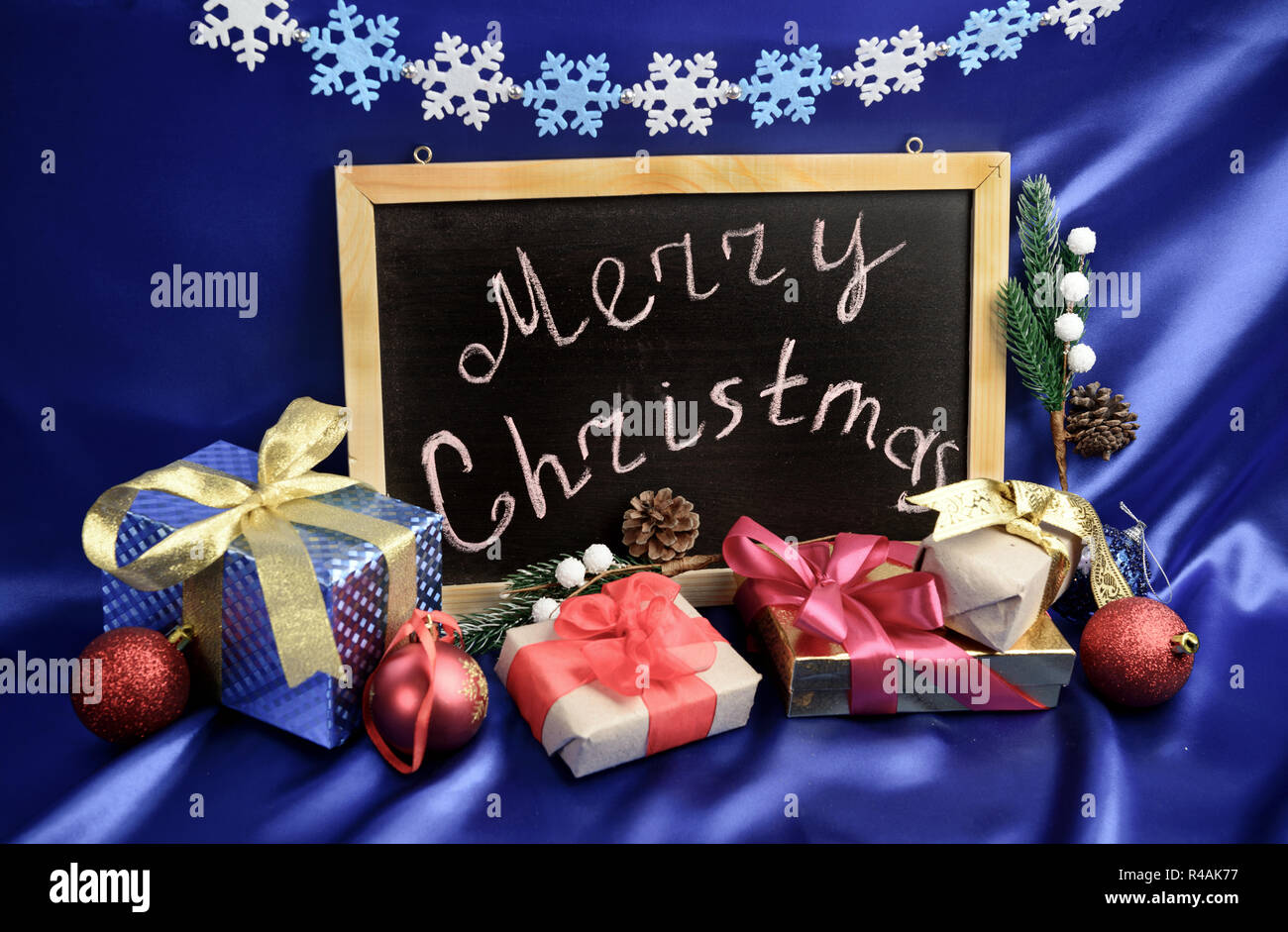 Christmas greeting at chalkboard around gift boxes and evergreen decorations on blue silk background Stock Photo