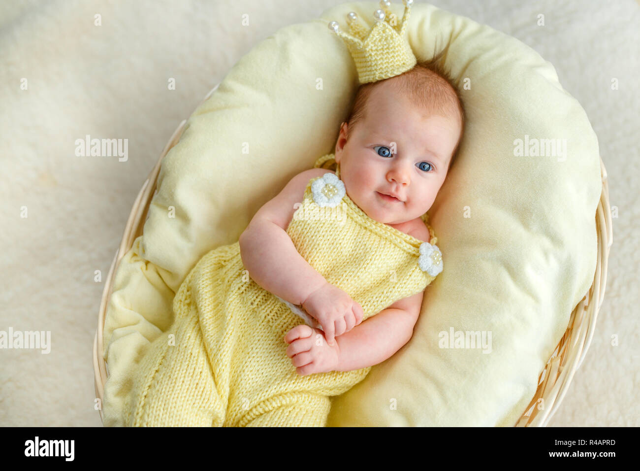 Newborn baby girl lying in a basket with crown and yellow bodysuit Stock Photo