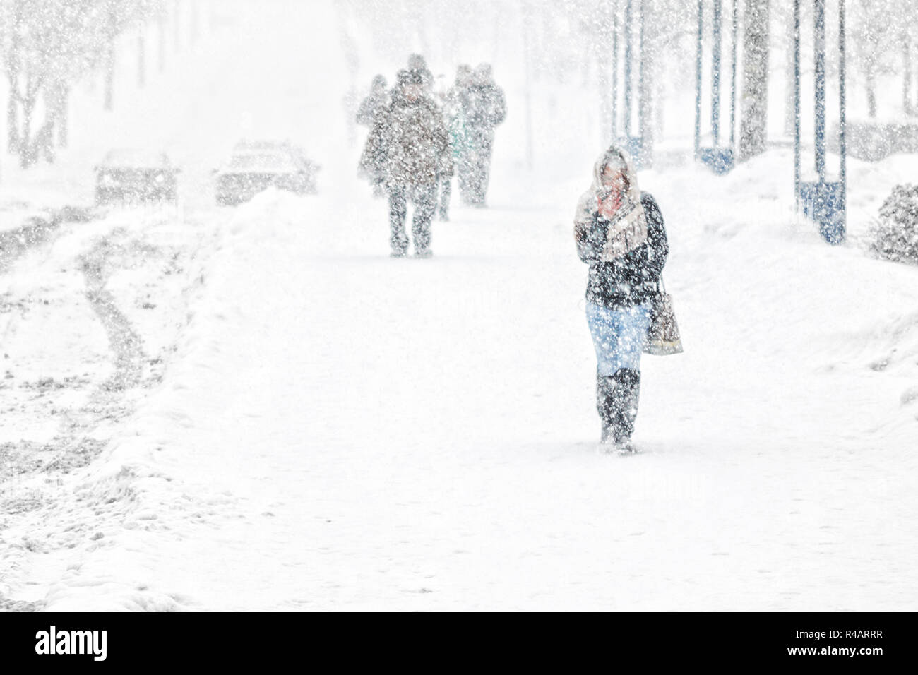 Young girl walk through snowfall resisting the pressure of a snowfall. Blizzard in an urban environment. Abstract blurry winter weather background Stock Photo