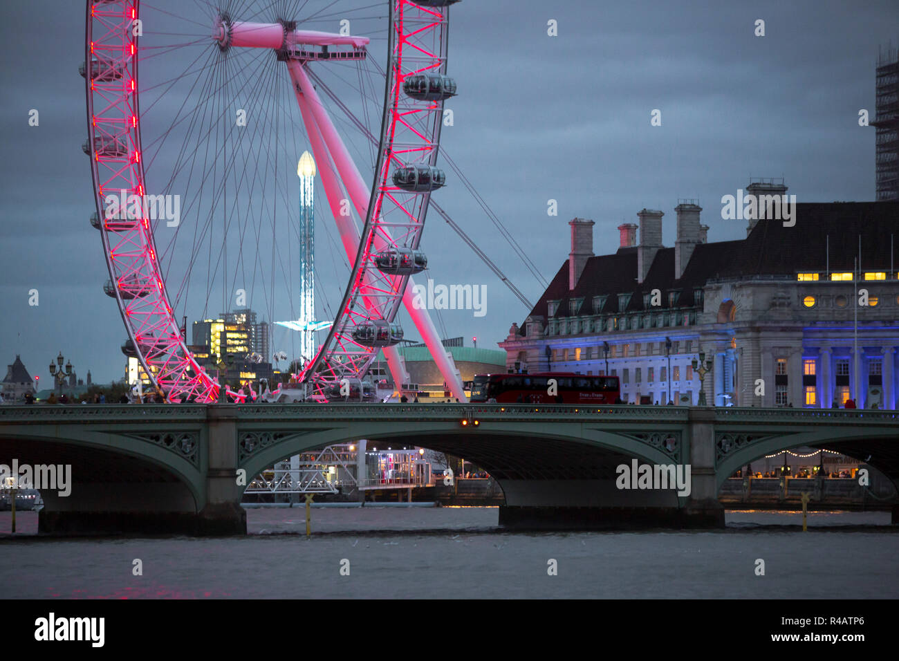 View of the Lodoon eye wheel on the banks of the River Thames in London illumintaed by red lights and set against a deep blue twilight sky with cloud in the autumn evening. Stock Photo