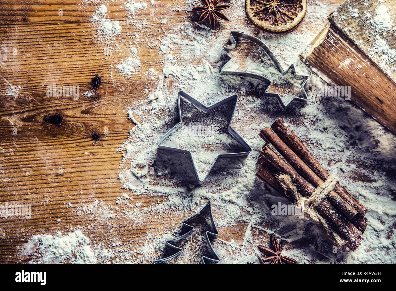 Top of view bakery table full of christmas aromatic ingredients star anise cinnamon dried orange flour cookery book and cookie cutters. Stock Photo