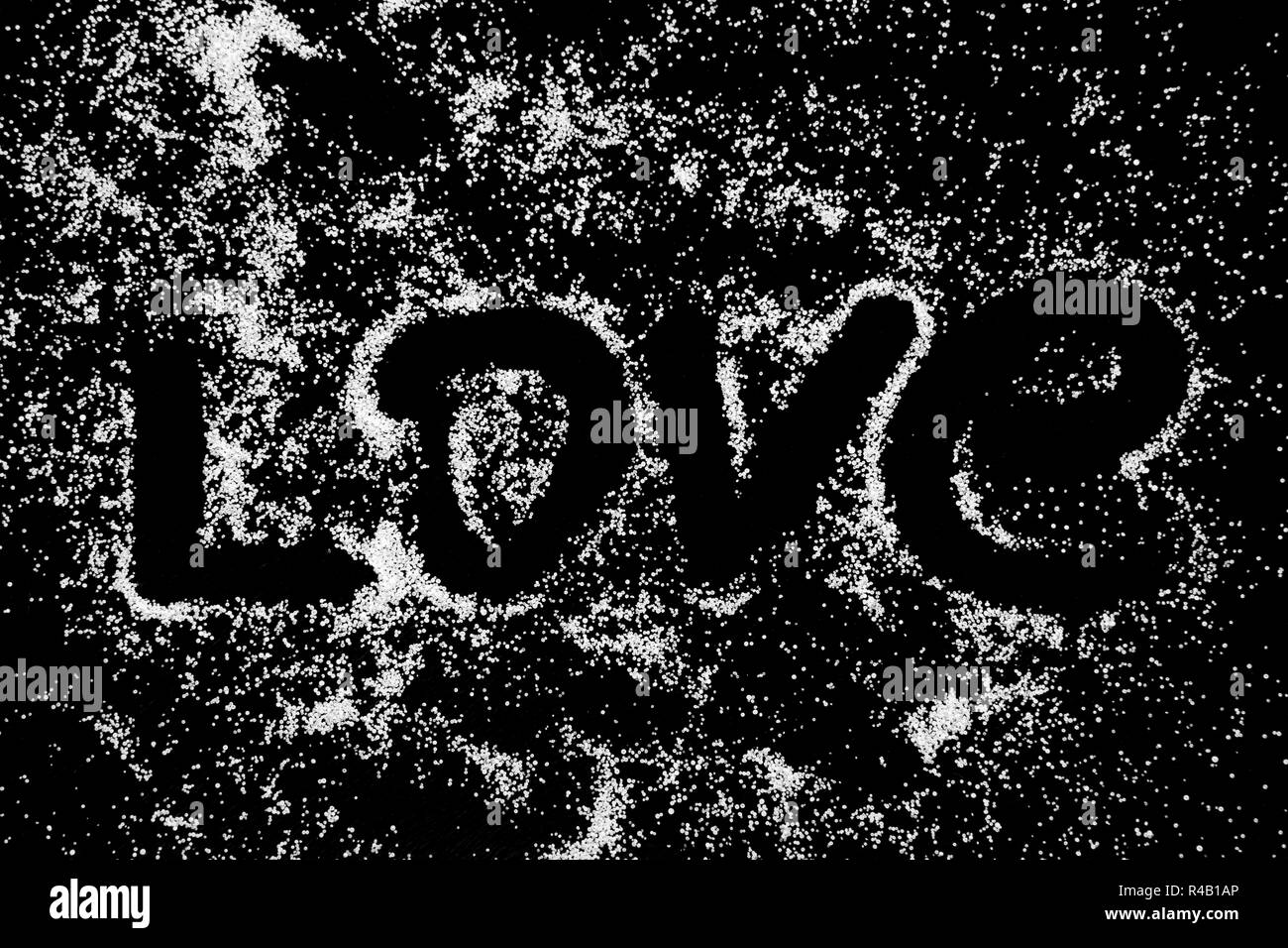 Love word symbol drawing by finger on white salt powder on black background. Capital and italics letters. Romantic St. Valentines Day holidays concept with place for text. Copy space. Stock Photo