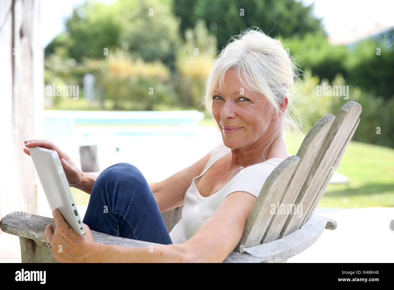 Senior woman reading book by swimming-pool Stock Photo - Alamy