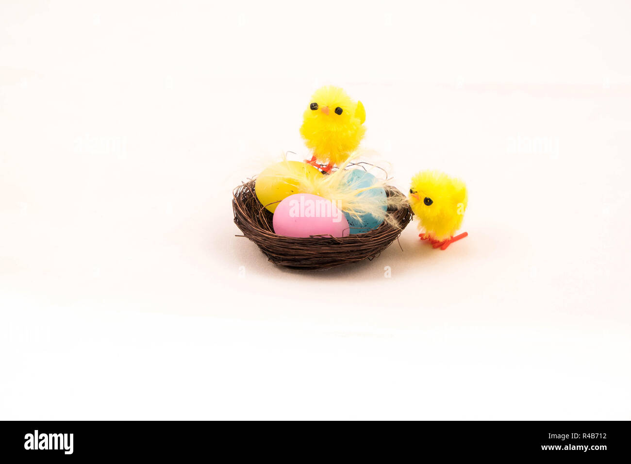 Easter fluffy toy chicks on nest with three eggs against white
