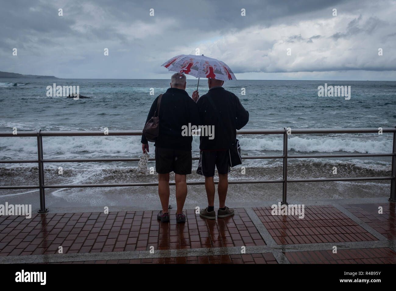Two persons with one humbrela under the rain in Las Canteras beach in LAs Palmas de Gran Canaria. Canary Island. Spain Stock Photo