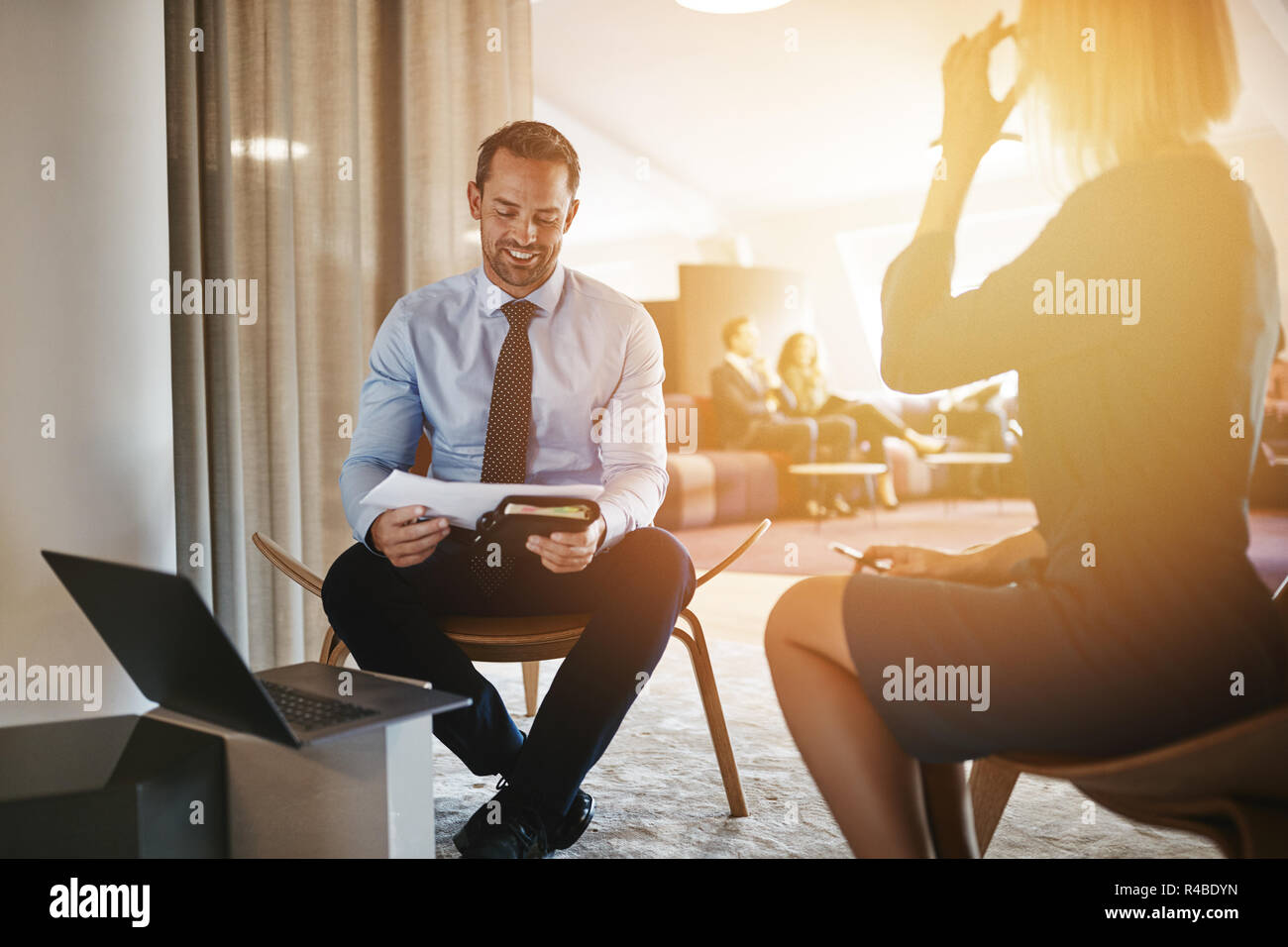 Two smiling young businesspeople going over paperwork together while sitting in a bright modern office Stock Photo