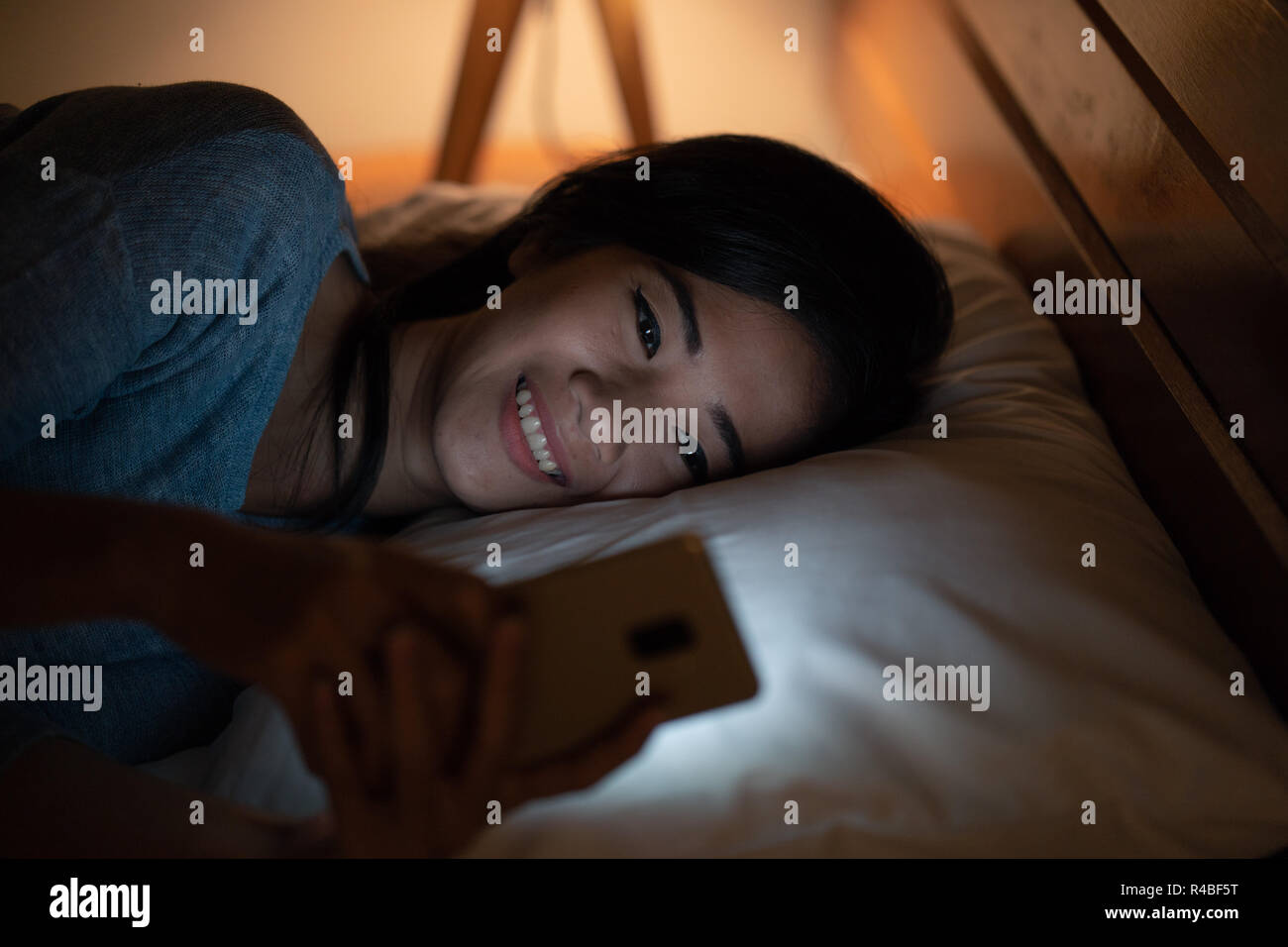 asian woman with smart phone while laying on bed Stock Photo - Alamy