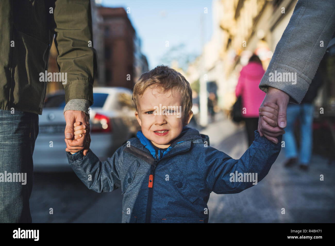 A small toddler boy with unrecognizable parents walking outdoors in city. Stock Photo