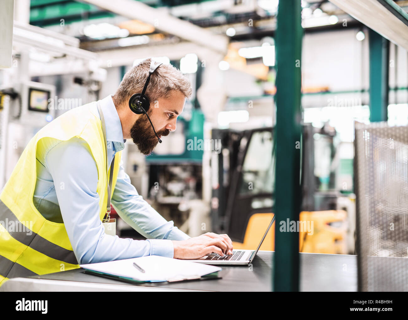 An industrial man engineer with headset and laptop in a factory, working. Stock Photo