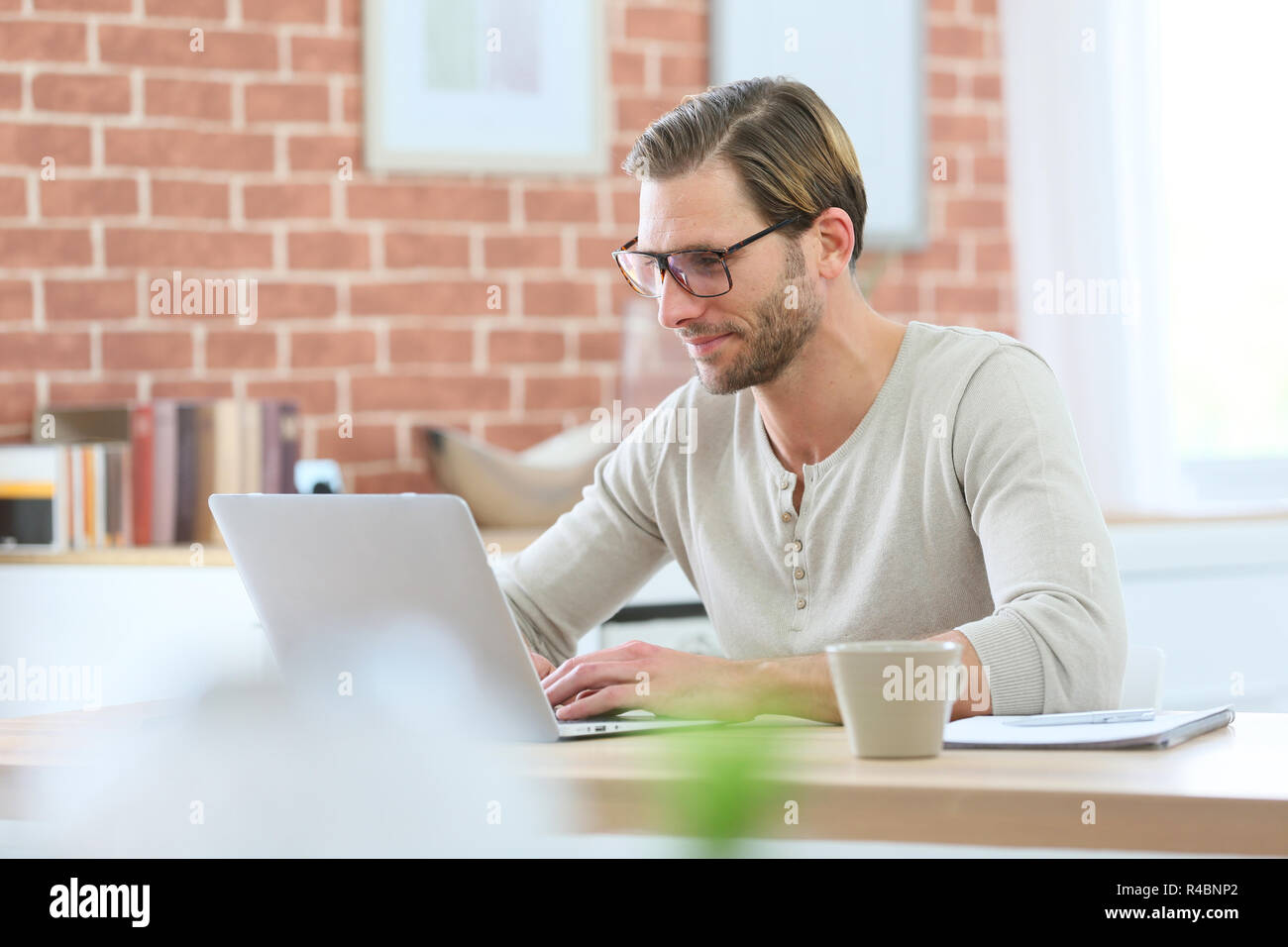 Blond guy with eyeglasses sitting in front of laptop computer at home ...
