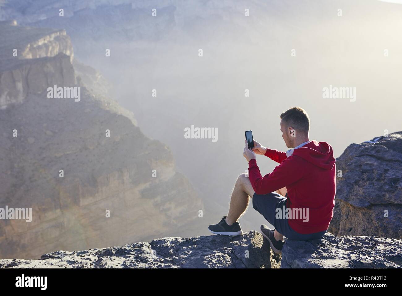 Relaxation in mountains. Young man photographing by mobile phone. Jebel Akhdar, Grand Canyon of Oman. Stock Photo