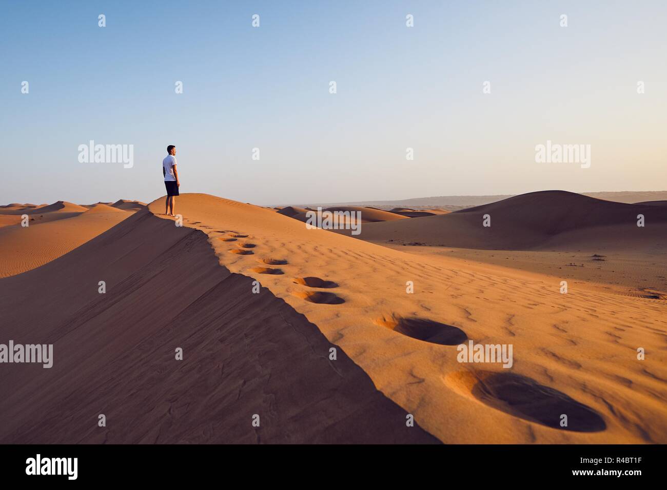 Young man standing on top of sand dune and looking at view. Desert Wahiba Sands in Oman. Stock Photo