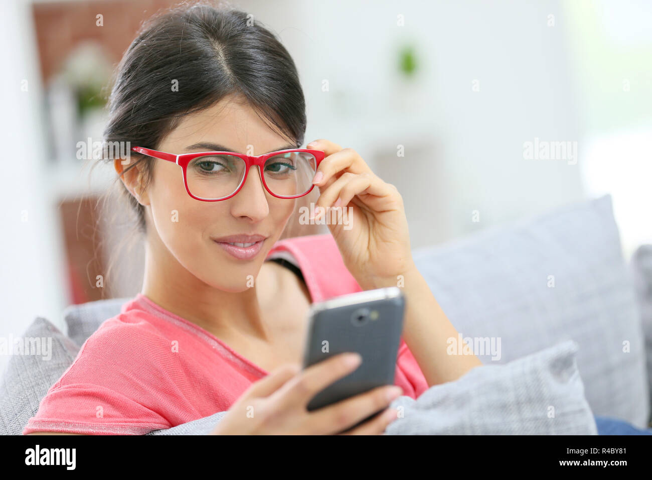 Brunette girl with red eyeglasses reading message on smartphone Stock Photo